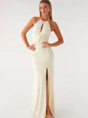 Lång ljus klänning med slits - Elegant långklänning i ljus färg med halterneck och snygg twist-detalj framtill. Klänningen har en hög slits framtill och är ärmlös, perfekt för speciella tillfällen. Materialet ser ut att vara mjukt och följsamt.