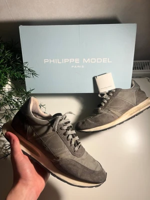 Grå Philippe Model sneakers - Snygga sneakers från Philippe Model i grått med vita detaljer. Skorna har klassisk snörning och en stilren design med paneler i mocka och syntet. Perfekta för dig som gillar en clean och trendig look.