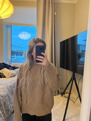 Beige stickad tröja från H&M - Mysig beige stickad tröja från H&M med hög krage och avslappnad passform. Tröjan har långa ärmar och är tillverkad i ett mjukt, ribbstickat material som passar perfekt för kyliga dagar.