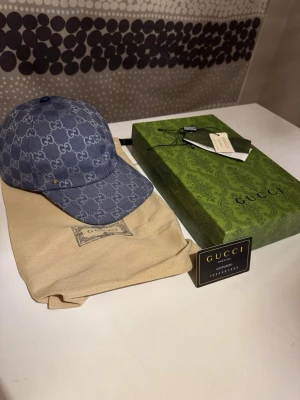 Gucci Dubai keps - Snygg blå keps från Gucci i denim med klassiskt GG-mönster över hela kepsen. Justerbar baktill och med beige insida. Kommer med originalförpackning, dustbag och äkthetskort. Perfekt accessoar för att lyfta din stil. Använd fåtal gånger, väldigt bra skick.