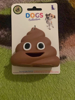 Hundbajspåsehållare & Fästingborttagare - Säljer en brun bajspåsehållare i form av en emoji från Dogs Collection samt en gul fästingborttagare från SkinOcare. Bajspåsehållaren har ett glatt ansikte och är gjord i plast. Fästingborttagaren är liten, smidig och passar både människor och djur.