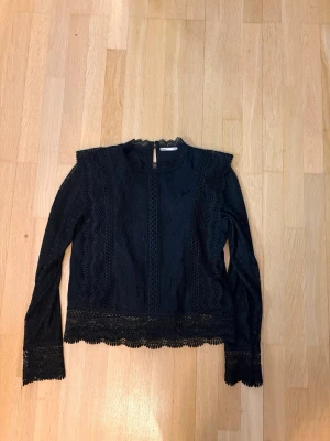 Svart spetsblus från ONLY - Pris kan diskuteras. Supersnygg svart spetsblus från ONLY med långärmad design och fina spetsdetaljer vid hals, ärmslut och nederkant. Blusen har rund halsringning och knäppning bak i nacken. Perfekt för dig som gillar en trendig och elegant look.