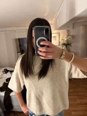 Beige stickad tröja från Arket - En stilren beige stickad tröja från Arket med korta ärmar och rund halsringning. Tröjan har en avslappnad passform och är gjord i ett mjukt, mysigt material som passar perfekt till jeans eller kjol.