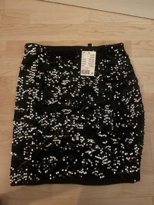 Svart paljettkjol från H&M - Snygg svart kortkjol från H&M täckt med glittriga paljetter. Kjolen har en tight passform och är perfekt för dig som vill sticka ut. Materialet är polyester och kjolen har en riktigt festlig vibe.