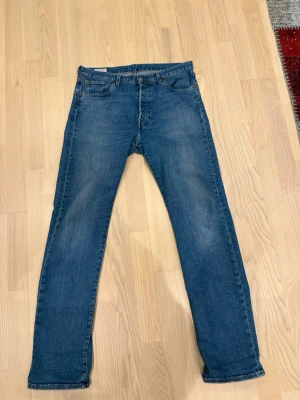 Blå raka jeans från Levi's - Klassiska blå jeans från Levi's med rak passform och fem fickor. Jeansen har en mellanblå tvätt och subtila slitningar framtill. Tillverkade i bomull med en tidlös look och läderpatch bak i midjan.