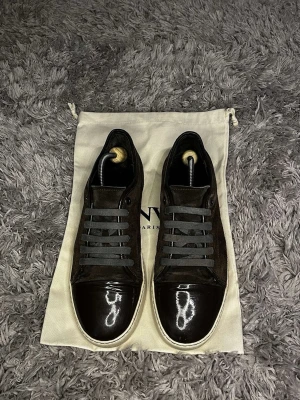Bruna sneakers från Lanvin - Snygga bruna sneakers från Lanvin med ovandel i mocka och detaljer i blankt skinn på tån. Skorna har grå snörning och vit platt sula. Perfekta för dig som gillar stilrena och exklusiva sneakers.priste kan diskuteras!!!