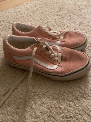 Vans Old Skool rosa sneakers - Säljer ett par klassiska Vans Old Skool sneakers i rosa mocka med vit sidestripe och vita snören. Skorna har låg profil och vit gummisula med svart rand. Perfekta för dig som gillar streetwear och vill ha en snygg och bekväm sko till vardags.