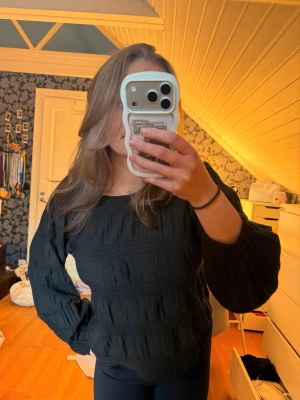Svart blus med vida ärmar - Säljer en svart blus med rund hals och vida, långa ärmar. Blusen har ett strukturerat tyg med diskreta horisontella sömmar som ger en cool look. Perfekt för dig som gillar stilrena och trendiga plagg.