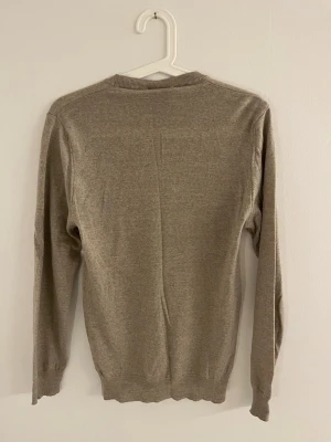 Beige stickad tröja från Oscar Jacobson - En stilren beige stickad tröja från Oscar Jacobson med rund halsringning och långa ärmar. Tröjan har ribbade muddar vid ärmslut, hals och nederkant. Perfekt för lager-på-lager och enkel att matcha med olika outfits.