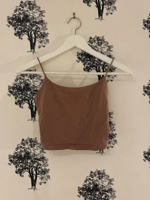 Brun croppad linnetopp - Snygg brun croppad linnetopp med tunna axelband. Perfekt för varma dagar och enkel att matcha med jeans eller kjol. Toppens enkla design gör den till ett måste i garderoben.