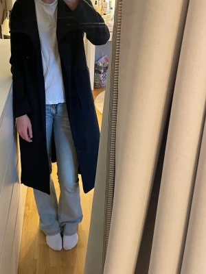 Svart lång kappa med skärp - Stilren svart lång kappa med skärp i midjan och bred krage. Kappan har en rak passform och går ner till knäna. Perfekt för kyligare dagar och enkel att matcha med olika outfits. Jag säljer eftersom den är för liten för mig😊