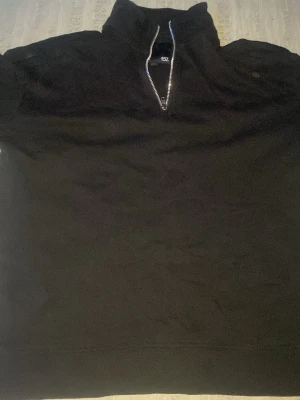 Svart cardigan tröja med hög krage - Säljer en svart halfzip tröja med hög krage och dragkedja framtill. Perfekt för lager på lager och enkel att matcha med olika outfits. Tröjan har en avslappnad passform och är tillverkad i mjukt material.