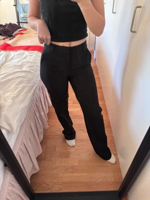 Svarta raka kostymbyxor - Snygga svarta kostymbyxor med rak passform och hög midja. Byxorna har klassisk design med hällor för skärp och diskreta fickor. Perfekta för en stilren look. Materialet känns mjukt och följsamt. Storlek 32. Jag är 160 och de är långa för mig. Har katter hemma så de kan hara lite håriga men kommer fixa innan ska posta. 