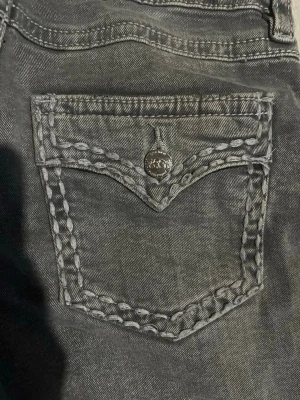 Grå  jeans med kontrastsömmar - Säljer ett par grå jeans från Gina tricot med deras ikoniska kontrastsömmar och snygga fickdetaljer med knapp. Jeansen har raka ben och klassisk femficksdesign. Perfekta för dig som gillar streetstyle och vill sticka ut lite extra.