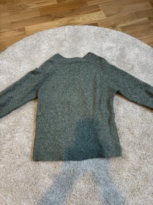 Grön stickad tröja - En enkel och stilren gråmelerad stickad tröja med rund halsringning och långa ärmar. Tröjan har ribbstickade muddar vid ärmslut och nederkant. Perfekt för lager-på-lager och passar till det mesta.