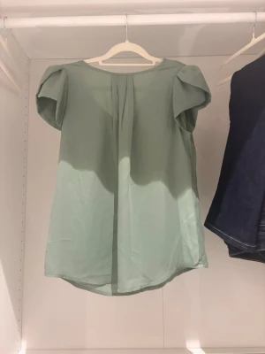 Ljusgrön blus med puffärmar - Snygg ljusgrön blus med korta puffärmar och rund halsringning. Blusen har en lös och luftig passform med ett mjukt fall. Perfekt att styla med jeans eller kjol för en trendig look.