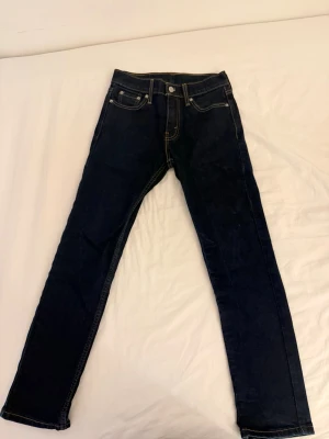 Mörkblå Levi's jeans med raka ben slim fit - Säljer ett par mörkblå Levi's jeans med klassisk femficksmodell och raka ben. Jeansen har kontrastsömmar och en ikonisk läderpatch bak i midjan. Perfekta för dig som gillar tidlös och enkel stil.