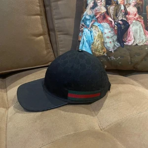 Svart Gucci keps - Säljer en autentisk svart keps från Gucci med diskret GG-monogram över hela kepsen och klassiska gröna och röda ränder på sidan. Pris kan diskuteras vid snabb affär