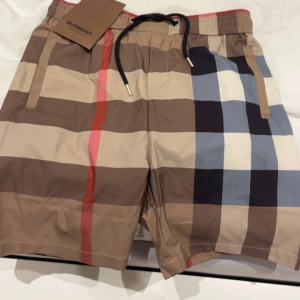 Burberry badshorts  - Säljer nu ett par fina burberry badshorts med prislapp kvar har inte använt dom än då jag aldrig hann, midjan är perfekt till kroppen och den formar sig efter midjan längden e super bra passar mig som är 176 cm lång, säljer billigt eftersom sommaren redan har passerat..