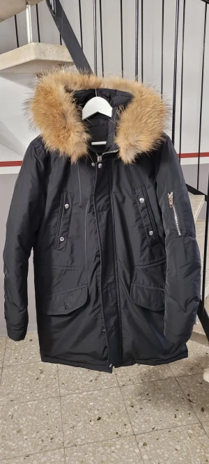 Svart parkas från Rockandblue med päls - Svart parkas från Rockandblue med stor fluffig päls runt huvan. Jackan har quiltad insida, dragkedja och knappar framtill, flera fickor och snygga detaljer som dragkedja på ärmen. Perfekt för kalla dagar med sin långa och loose passform.Top skick storlek M 