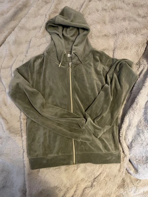 Grön velour hoodie från Gina Tricot - Mjuk och chill grön hoodie i velour från Gina Tricot. Tröjan har huva med snörning, hel dragkedja framtill och långa ärmar. Perfekt för dig som gillar comfy vibes och vill ha något snyggt och enkelt att slänga på sig.