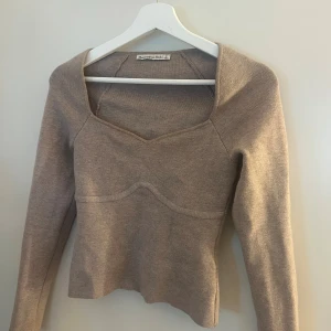Beige stickad tröja Abercrombie S - Supersnygg beige stickad tröja från Abercrombie & Fitch i storlek S. Tröjan har långärmad design, markerad söm över bröstet och en cool fyrkantig halsringning som ger en modern vibe. Perfekt att styla med jeans eller kjol för en chill look.