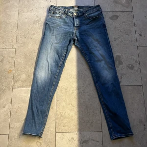 Slim Glenn jeans från Jack & Jones - Snygga blå Slim Glenn jeans från Jack & Jones med klassisk femficksdesign och kontrastsömmar. Modellen har slim passform och raka ben, tillverkade i mjukt jeanstyg. Perfekt för dig som gillar en modern och stilren look.