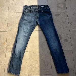 Slim Glenn jeans från Jack & Jones - Mörkblå jeans från Jack & Jones, modell Slim Glenn. Snygg slim fit med klassisk femficksdesign och kontrastsömmar. Jeansen har normal midja och raka ben, tillverkade i slitstarkt bomullsmaterial med dragkedja och knappstängning.