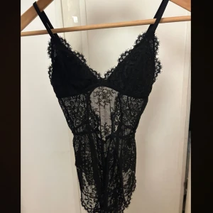 H&M spetsbody - Supersnygg svart spetsbody med v-ringad urringning och tunna axelband. Bodyn  är genombruten med blommigt spetsmönster och har en figurnära passform som framhäver midjan. Perfekt för dig som gillar en lite mer vågad och trendig look.