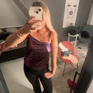 Lila glansig linne-topp med smala band - Säljer en lila glansig linne-topp med smala axelband och snygg drapering framtill. Toppen har en metallic finish som verkligen sticker ut och ger en cool vibe. 