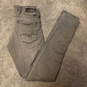 Replay grå jeans slim fit - Snygga Replay Anbass jeans i grått med slim fit och klassisk femficksdesign. Jeansen har svarta kontrastsömmar, logotyp på bakfickan och bekvämt stretchmaterial. Passar dig som gillar stilrena och moderna jeans. Är i väldigt fin skick. Hör av vid frågor, pris kan disskuteras;))