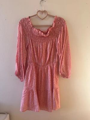 Rosa kortklänning från H&M, S - Supersöt rosa kortklänning från H&M med vitt bladmönster, smockad överdel och trekvartsärmar. Klänningen har volangkant nertill och är gjord i mjuk bomull, perfekt för varma dagar. Säljs i storlek S.