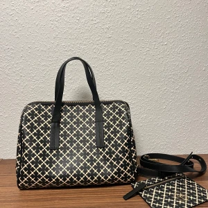 Mönstrad handväska By Malene Birger - Snygg handväska från By Malene Birger med svart och beige grafiskt mönster. Väskan har svarta handtag, guldfärgad dragkedja och medföljande matchande plånbok. Tillverkad i slitstarkt syntetmaterial och har en boxig form som rymmer allt du behöver.