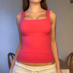 Rosa ribbad linnetopp  - Säljer en snygg rosa linnetopp med breda axelband och fyrkantig halsringning. Toppen är ribbad och har en tight passform som framhäver figuren. Perfekt för dig som gillar färg och vill ha en enkel men trendig topp till sommaren.