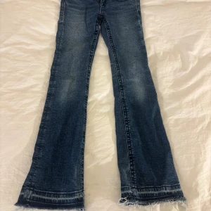 Blå bootcut jeans från Gina Tricot - Snygga blå jeans från Gina Tricot med bootcut passform och fransade. Jeansen har silverknappar med fina fickor. Jeansen är lågmidjade och är tillverkade i jeansmaterial.