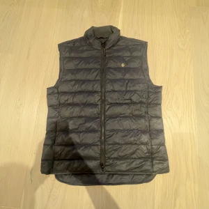 Morris väst  - Säljer en mörkblå väst från Morris i storlek Small. Perfekt för lager-på-lager och snygg att styla till både hoodie och skjorta. Klassisk Morris-logga på bröstet och stilren look. Västen har däremot en liten skada på ryggen men syns inte så mycket och går att laga. Nypris ligger på 2299