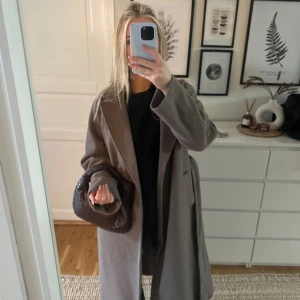 Beige omlott kappa med bälte - Säljer en snygg beige kappa med omlott-design och bälte i midjan. Jackan har långärmade ärmar, bred krage och en loose passform.