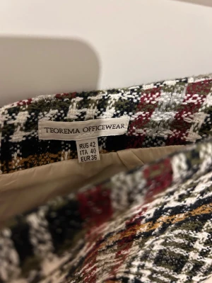Rutig kjol från Teorema Officewear - Snygg rutig kjol från Teorema Officewear i klassisk pennkjolsmodell. Färgerna är svart, vit, röd och inslag av gul och grön. Kjolen är fodrad och har en strukturerad yta som ger en cool vibe. Perfekt för dig som gillar preppy och stilrena outfits.