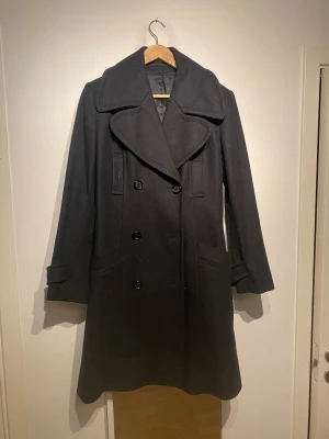 Svart rock från Tiger of Sweden - Svart rock från Tiger of Sweden. Jackan har långa ärmar med knappdetalj vid mudden och två stora fickor framtill. Materialet är ull och insidan är fodrad med satin för extra komfort. Perfekt för kyliga dagar. Bra nu för vintern!!