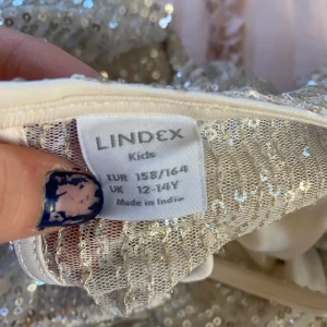 Glittrig topp från Lindex - Säljer en glittrig topp från Lindex i ljusbeige med paljetter över hela. Toppen har korta volangärmar och rund halsringning. Perfekt för dig som vill sticka ut lite extra!