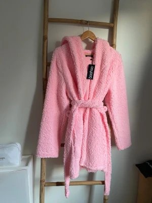 Morgonrock  - Supermysig rosa morgonrock från Boohoo med stor huva och knytbälte i midjan. Långärmade ärmar och fluffigt, mjukt material som ger en chill vibe. Perfekt för dig som vill ha en cozy look och gillar pastellfärger. ALDRIG ANVÄND!🤩
