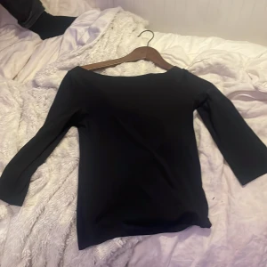 Svart långärmad topp med båtringning - Snygg svart topp med båtringad hals och lång ärm. Enkel och stilren design som passar till många olika looks. Materialet känns mjukt och stretchigt, vilket gör den bekväm att bära. Perfekt att matcha med jeans eller kjol för en clean vibe.