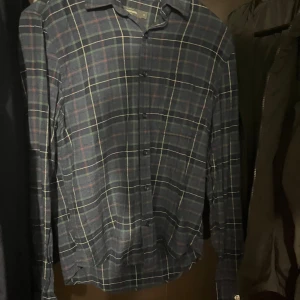  rutig skjorta  - Snygg mörkblå skjorta från dressman med rutigt mönster i grönt, vitt och rött. Skjortan har klassisk krage, långa ärmar och knäppning framtill. Perfekt för dig som gillar en chill och stilren look.