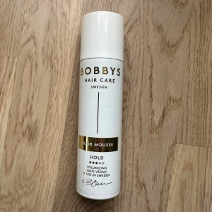 Bobbi's Hair Mousse Volumizing - Volymgivande hårmousse från Bobbys Hair Care Sweden i vit flaska med gulddetaljer. Produkten är 100% vegansk och tillverkad i Sverige, med extra stadga för att ge håret fyllighet och hållbarhet.