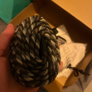 Svarta och gråa skosnören - Säljer ett par snygga, tjocka skosnören i svart och grått med tvinnad design. Perfekt för att ge dina sneakers eller kängor en unik look. Passar till både sportiga och vardagliga skor.