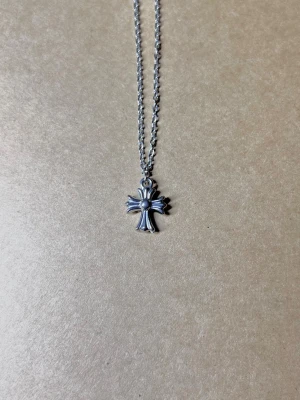 Croix Minimaliste Rebelle - Ett stilrent silverhänge i form av ett kors som mäter 1,3 x 1,1 cm. Hänger på en 50 cm lång kedja med en bredd på 1,5 mm. Halsbandet är tillverkat i rost- och nickelfritt material för optimal komfort och hållbarhet.