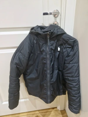 Grå jacka från The North Face - Säljer en grå pufferjacka från The North Face med huva och quiltad design. Jackan har två olika grå nyanser, dragkedja framtill och en extra ficka med dragkedja på bröstet. Perfekt för kalla dagar och har en clean streetstil. Man kan välja om man vill ha den grå eller svart beroende om man vänder jackan ut och in. Kom med pris förslag