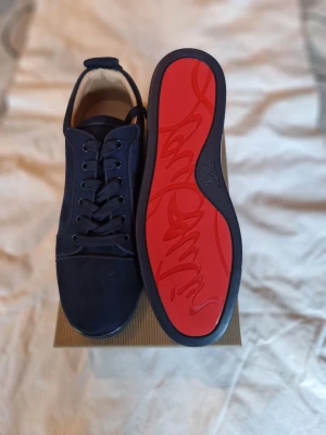 Mörkblå Christian Louboutin sneakers - Snygga mörkblå sneakers från Christian Louboutin i mocka med klassisk röd sula och broderad logga på hälen. Skorna har rund tå, platt sula och snörning framtill. Perfekta för dig som vill sticka ut med exklusiva detaljer och lyxig känsla. Låda ingår ej här.