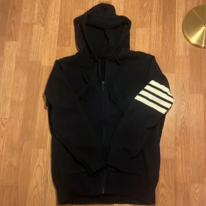 Svart hoodie med segelbåt och ränder - Snygg mörkblå hoodie med huva och dragkedja, stickad i mjukt material. Snygg segelbåtsdesign på ryggen och snygga tre ränder på ena ärmen. Aldrig använd.  Tveka inte på att skriva ifall du undrar nåt!✨