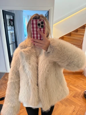 Beige fluffig pälsjacka - Säljer en supermysig och fluffig pälsjacka i beige ton. Jackan har lång ärm, bred krage och är oversized i modellen. Perfekt för dig som vill ha en statementjacka med lyxig känsla och extra volym. Jackan är helfärgad och har ett stilrent, enkelt uttryck.